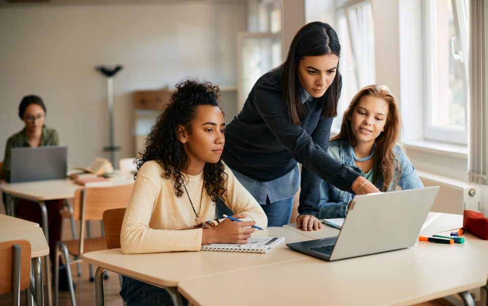 Female Teacher Clearing Doubts Of 2 Girls on Laptop in School Classroom